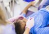 Atendimento odontológico de crianças diminui em 88% na pandemia; imagem mostra mão de dentista com luva mexendo na boca de menino sentado em cadeira de consultório