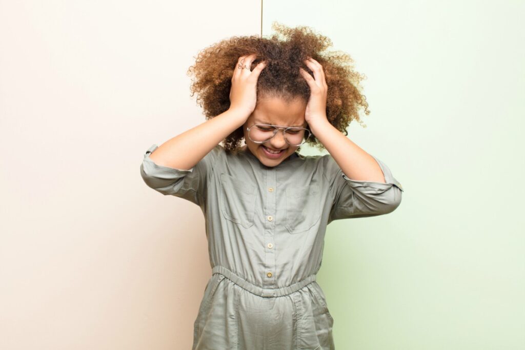 Dor de cabeça nas crianças: saiba as 4 causas mais comuns; imagem mostra garota de cabelos crespos com as mãos na cabeça e expressão de dor