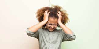 Dor de cabeça nas crianças: saiba as 4 causas mais comuns; imagem mostra garota de cabelos crespos com as mãos na cabeça e expressão de dor
