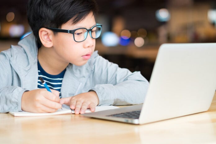 Resolução do CNE aprovada hoje permite aulas online até o fim de 2021; imagem mostra garoto de cabelo preto e óculos olhando para tela de computador
