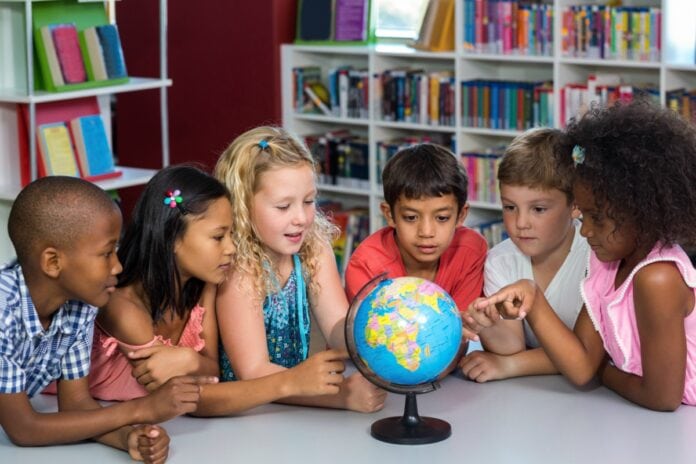 Mapa literário instiga crianças a desvendar tesouros da literatura brasileira; imagem mostra 6 crianças em mesa olhando para o mapa mundi
