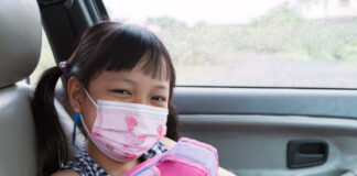 Menina oriental usando máscara infantil no carro