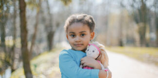 menina pequena de roupa azul abraça boneca em parque