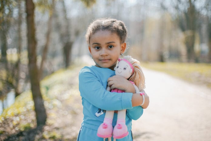 menina pequena de roupa azul abraça boneca em parque