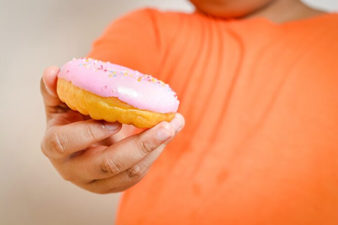 Obesidade infantil aumenta risco de fraturas em idade escolar; imagem mostra peito e barriga de menino gordo segurando um donut coberto de morango