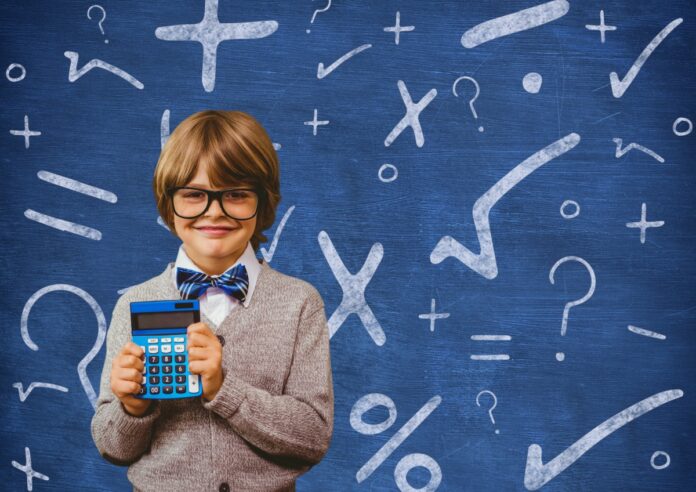 3 a cada 4 pais dizem já saber a carreira que os filhos irão seguir; imagem mostra garoto de óculos, terno e gravata borboleta azul segurando uma calculadora, ao fundo uma lousa azul tem símbolos matemáticos escritos