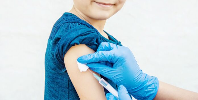 Coberturas vacinais: metade das vacinas infantis não atinge meta desde 2015; imagem mostra mão com luva azul emborrachada aplicando dose de vacina em braço de criança de blusa azul