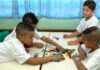 Retorno às escolas na rede pública de São Paulo terá baixa adesão; imagem mostra quatro alunos sentados mexendo em pecas de jogo sobre mesas