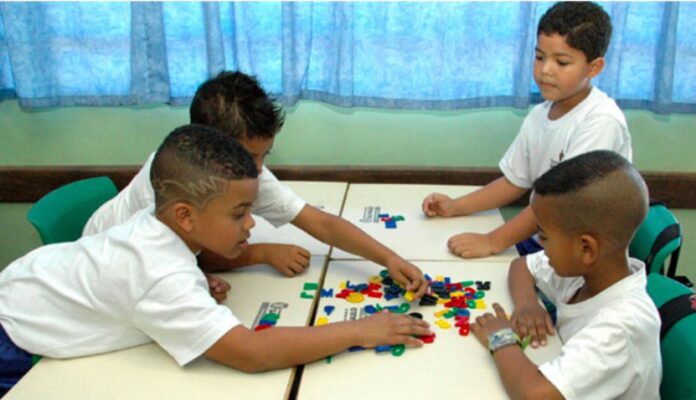 Retorno às escolas na rede pública de São Paulo terá baixa adesão; imagem mostra quatro alunos sentados mexendo em pecas de jogo sobre mesas
