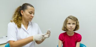 São Paulo faz campanha para melhorar índices de vacinação infantil; imagme mostra mulher de bata branca mexendo em seringa e criança sentada seu lado