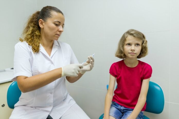São Paulo faz campanha para melhorar índices de vacinação infantil; imagme mostra mulher de bata branca mexendo em seringa e criança sentada seu lado