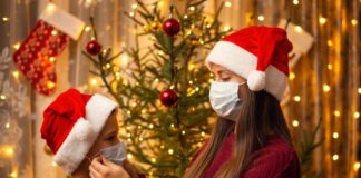CDC divulga guia com orientações para as festas de fim de ano; imagem mostra irmã mais velha de toca de Natal colocando máscara em irmão mais novo, que também usa toca natalina