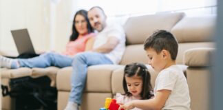 Por que pais preferem empregos estáveis ao empreendedorismo para os filhos; pais sentandos no sofá olham para os dois filhos brincando com peças de montar no chão
