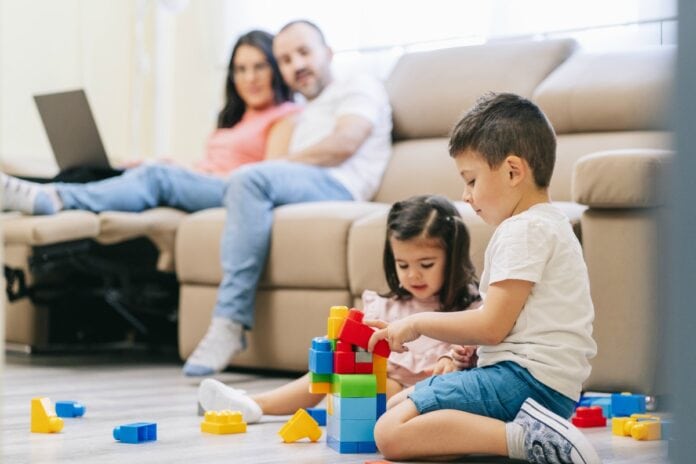 Por que pais preferem empregos estáveis ao empreendedorismo para os filhos; pais sentandos no sofá olham para os dois filhos brincando com peças de montar no chão