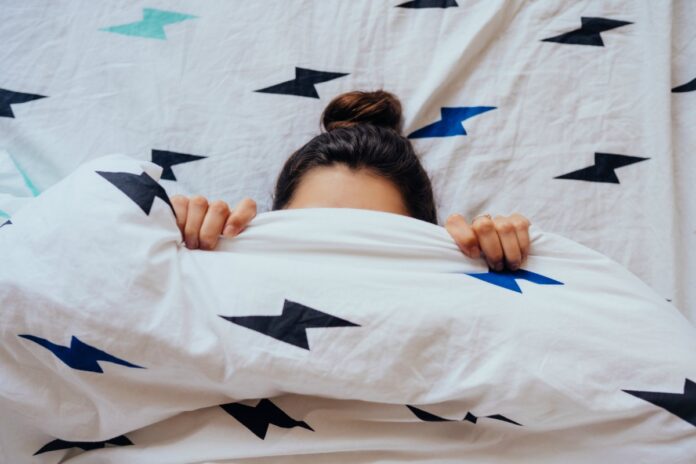 Preguiça: um vilão necessário; imagem mostra rosto de mulher na cama coberto por edredon até metade da testa