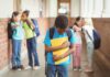 Um em cada três alunos em todo o mundo foi vítima de bullying na escola; imagem mostra menino de cabeça baixo em corredor de escola e 4 colegas cochichando ao fundo