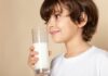 Diagnóstico de APLV pode demorar mais de três meses, diz estudo; menino segura copo de leite na mão