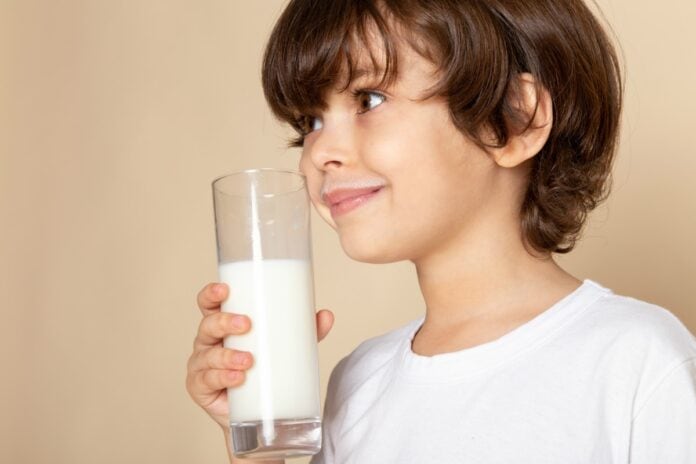 Diagnóstico de APLV pode demorar mais de três meses, diz estudo; menino segura copo de leite na mão