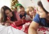 Cuidar da saúde mental é essencial para passar por esse período conturbado de forma harmoniosa; mãe, pai e dois filhos estão deitados na cama sob manta natalina e árvore de Natal ao fundo