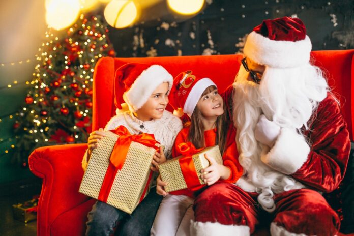 Como Papai Noel pode ajudar na educação financeira das crianças; crianças com gorro de Natal e presente nas mãos conversam com Papai Noel