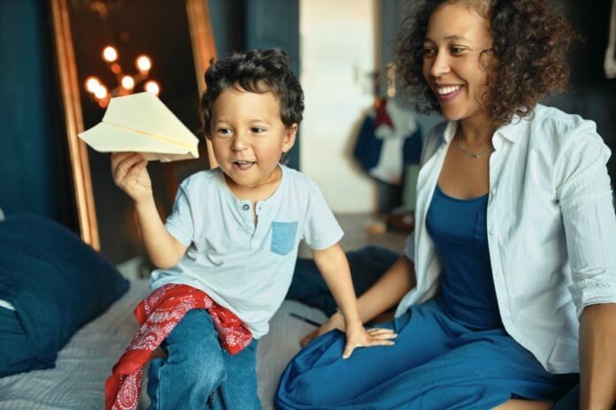 Fazer menos e melhor – mais simples, prático, e bonito; mãe olha sorridente para filho que segura aviãozinho de origami na mão