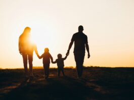É hora de fazer um balanço e repensar as prioridades; mãe, pai e dois filhos caminham ao ar livre com pôr do sol ao fundo