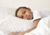 4 maneiras como o racismo afeta o cérebro da criança, segundo Harvard; Menino negro triste deitado em cima de travesseiro