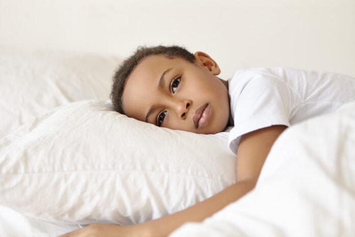 4 maneiras como o racismo afeta o cérebro da criança, segundo Harvard; Menino negro triste deitado em cima de travesseiro