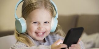 Compras online sem permissão: como evitar que isso aconteça?; menina com fones de ouvido e celular na mão olha sorridente para a câmera