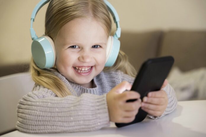 Compras online sem permissão: como evitar que isso aconteça?; menina com fones de ouvido e celular na mão olha sorridente para a câmera