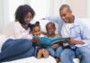 33% das crianças menores de 3 anos usam telas todos os dias, diz estudo; imagem mostra mãe e pai negros lendo livro junto com os dois filhos no sofá