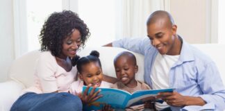33% das crianças menores de 3 anos usam telas todos os dias, diz estudo; imagem mostra mãe e pai negros lendo livro junto com os dois filhos no sofá