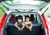 Viagem de carro em família: dicas para um passeio tranquilo (e divertido!); duas meninas estão de joelhos no banco traseiro de um carro olhando para trás com o porta malas aberto