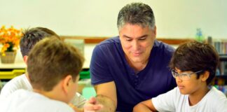 Professor vence prêmio de educação científica do Rio; professor conversa com 3 alunos sobre mesa