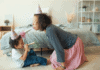 Desejo para 2021: saúde e compromisso com a infância; mãe e filho brincam no chão ao lado da cama, ambos com chapéu de cone na cabeça