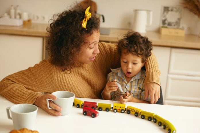Rotina com atividades divertidas ajuda a evitar depressão infantil; mãe brinca com filho na mesa da cozinha que tem duas canecas e trenzinho de brinquedo