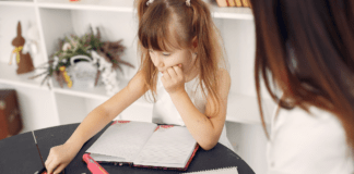 Menina sentada na mesa com cadernos e lápis tendo aula com professora particular