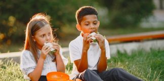 Alimentos fora de casa – na escola, por escola, por exemplo – pode ter proteger contra doenças crônicas, diz estudo; menino e menina comem lanche no gramado