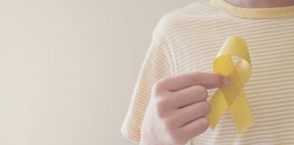 Câncer em crianças: saiba os sintomas aos quais ficar atento; mão de criança segura fitinha amarela que simboliza o mês de fevereiro e a luta contra o câncer infantojuvneil