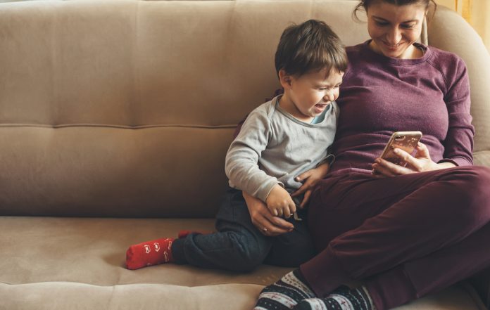Os aprendizados que os filhos levarão da pandemia depende de como os pais lidam com ela; mãe e filho estão no sofá e olham sorridentes para tela de celular