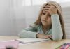 Estresse tóxico e estresse positivo: como eles afetam os pequenos; menina está sentada com mão na testa e outro sobre caderno sob a mesa
