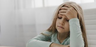 Estresse tóxico e estresse positivo: como eles afetam os pequenos; menina está sentada com mão na testa e outro sobre caderno sob a mesa