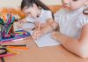 Importância da escrita à mão para o desenvolvimento das crianças; duas meninas escrevem em papel sobre mesa
