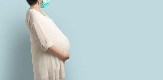Grávidas repassam anticorpos da Covid-19 aos bebês, indica estudo; mulher grávida de vestido branco e cabelo curto estende braço por baixo da barriga e usa máscara