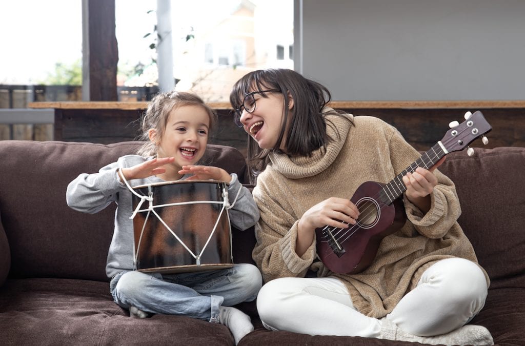Como despertar nas crianças o interesse por um instrumento musical; mãe toca instrumento de cordas e filha outro de percussão