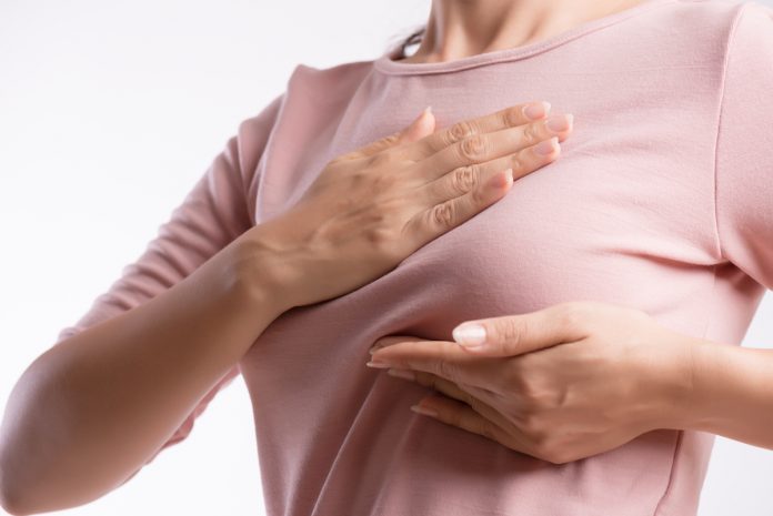 Exames de mamografia tiveram queda de mais de 60% em 2020; mulher de blusa rosa apalpa o seio