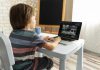 O primeiro dia de aula online; menino está sentado em escrivaninha olhando para professor em tela de computador