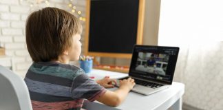 O primeiro dia de aula online; menino está sentado em escrivaninha olhando para professor em tela de computador