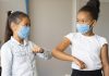 Como ajudar seu filho a se readaptar à rotina escolar; duas meninas de máscaras se cumprimentam tocando os cotovelos
