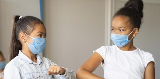Como ajudar seu filho a se readaptar à rotina escolar; duas meninas de máscaras se cumprimentam tocando os cotovelos